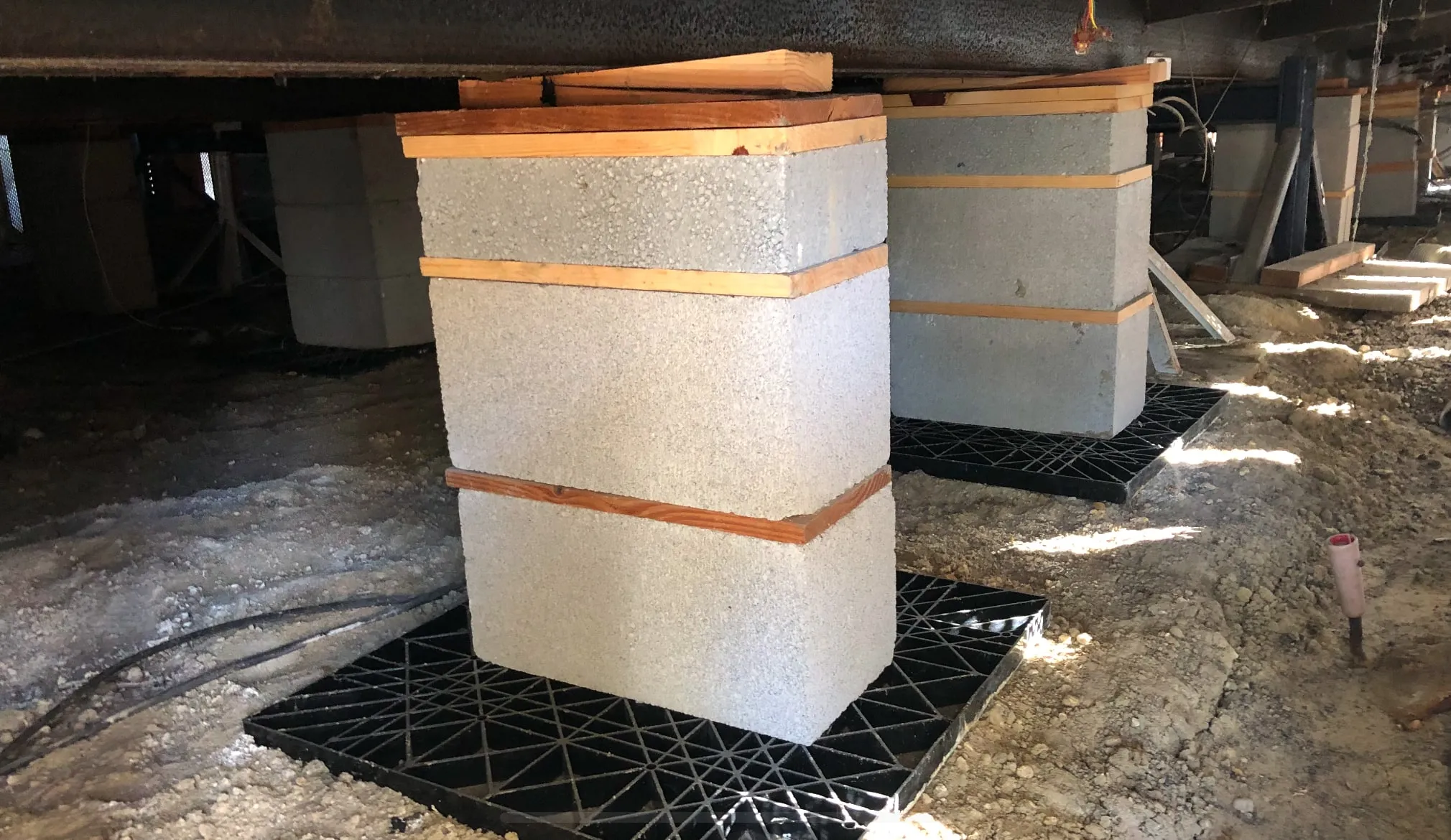 New concrete block piers with wood caps and shims on pier pads under a mobile home